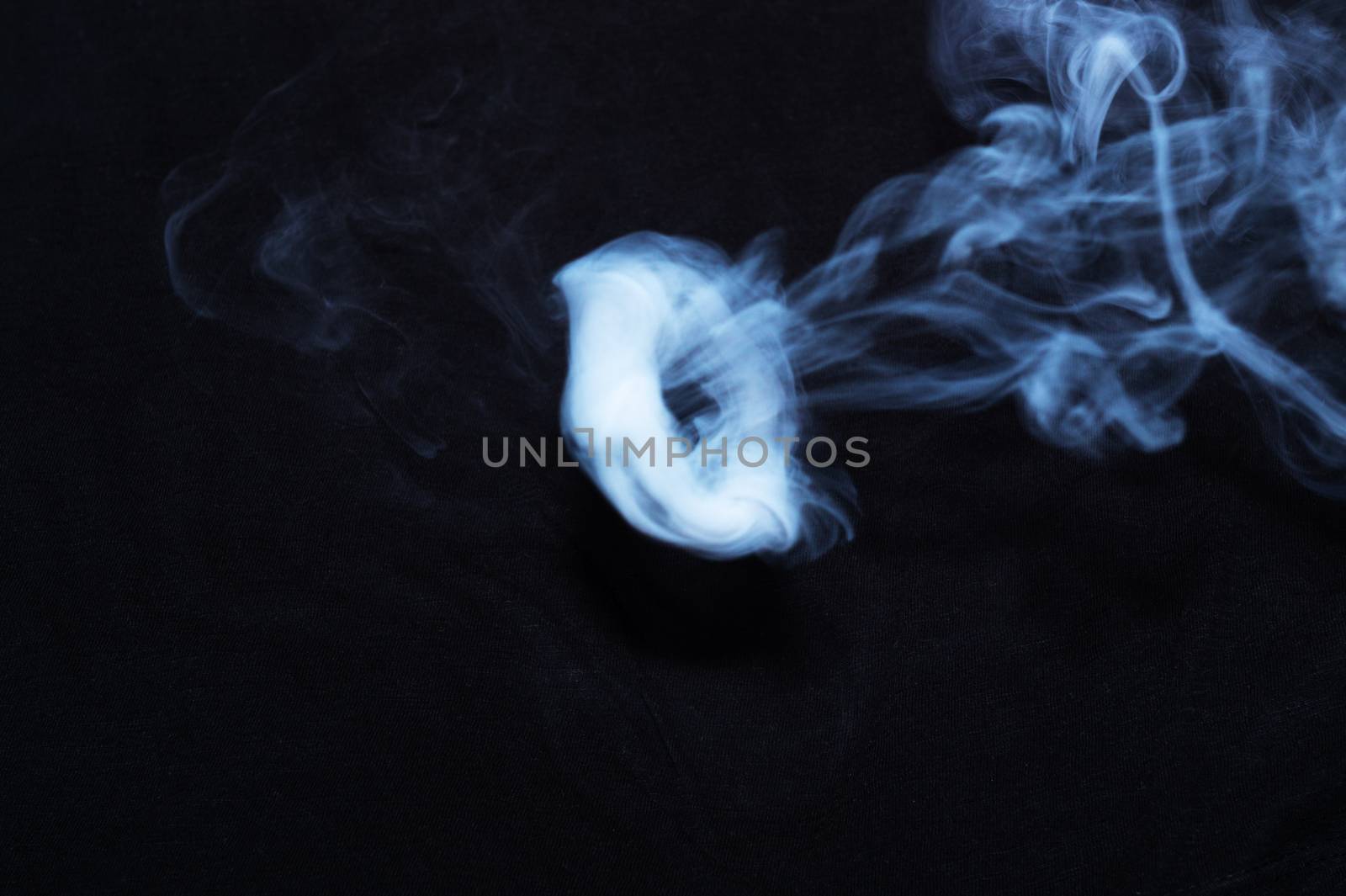 White smoke ring on black fabric background. Smoke spreads over the background. Vaping culture, life without cigarettes. Conceptual image.
