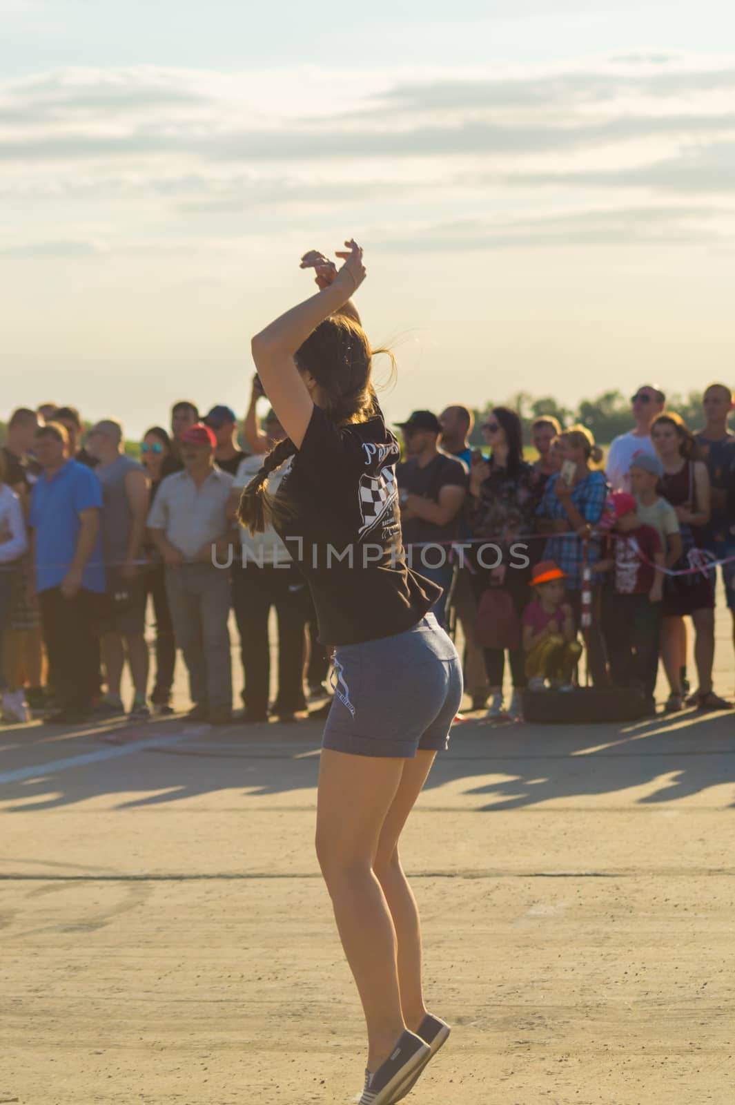 A girl in shorts and a T-shirt waving riders at the race signal for a jump start.