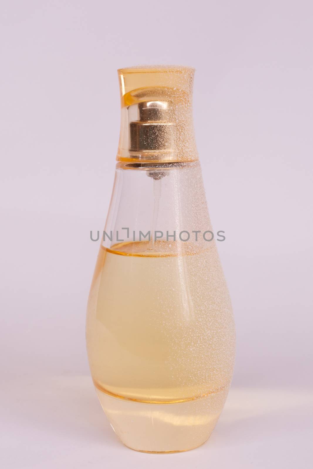 Warm yellow colour glass parfum bottle with artificial snow on white-purple background. Closeup view.