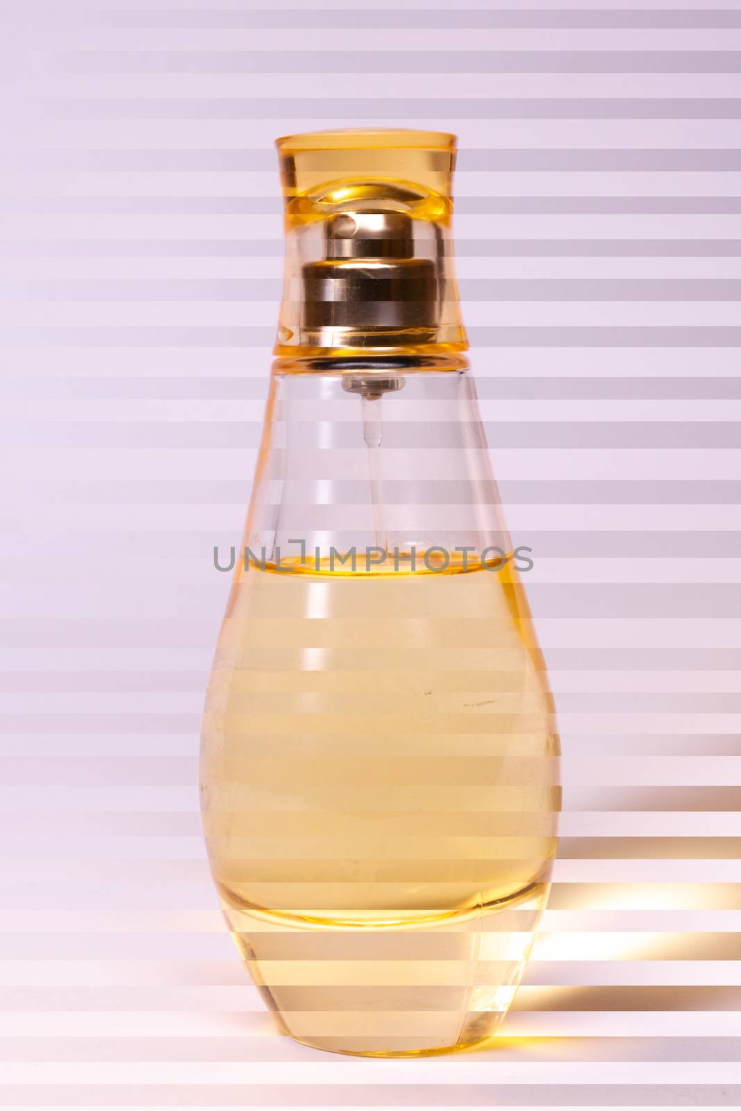 Warm yellow colour glass parfum bottle on white-purple background. Photo contains stripes.