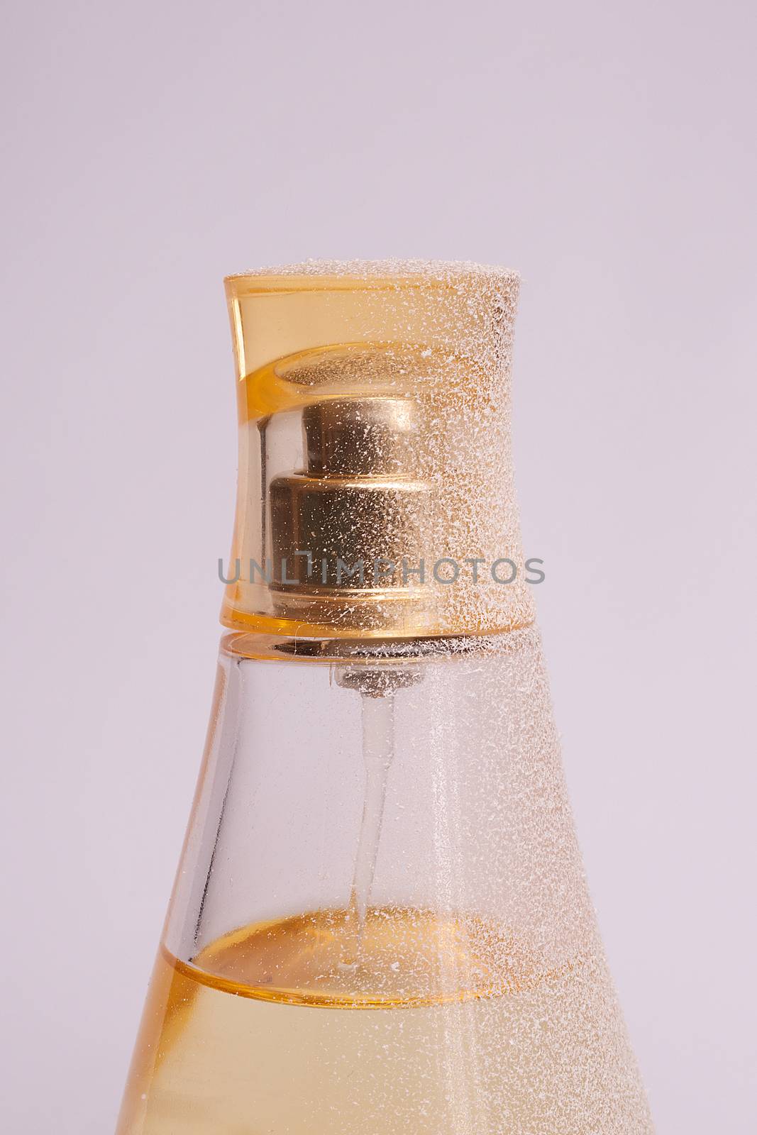 Warm yellow colour glass parfum bottle with artificial snow on white-purple background. Closeup view.