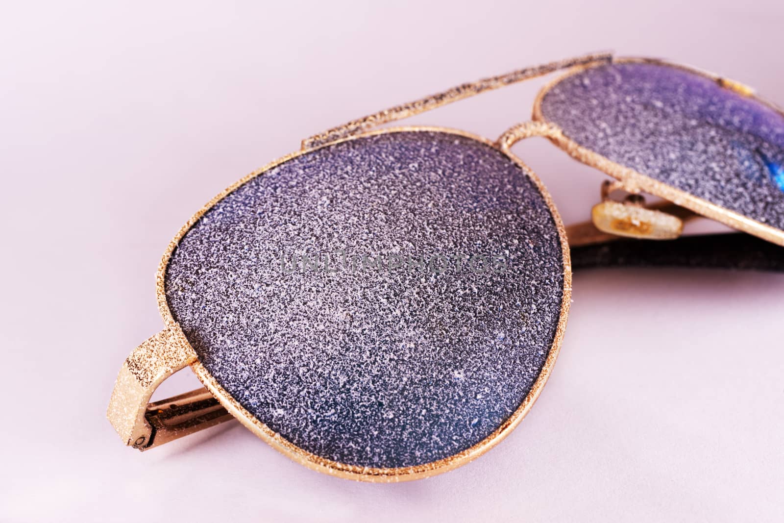 Sunglasses with artificial snow on white-purple background close-up view.