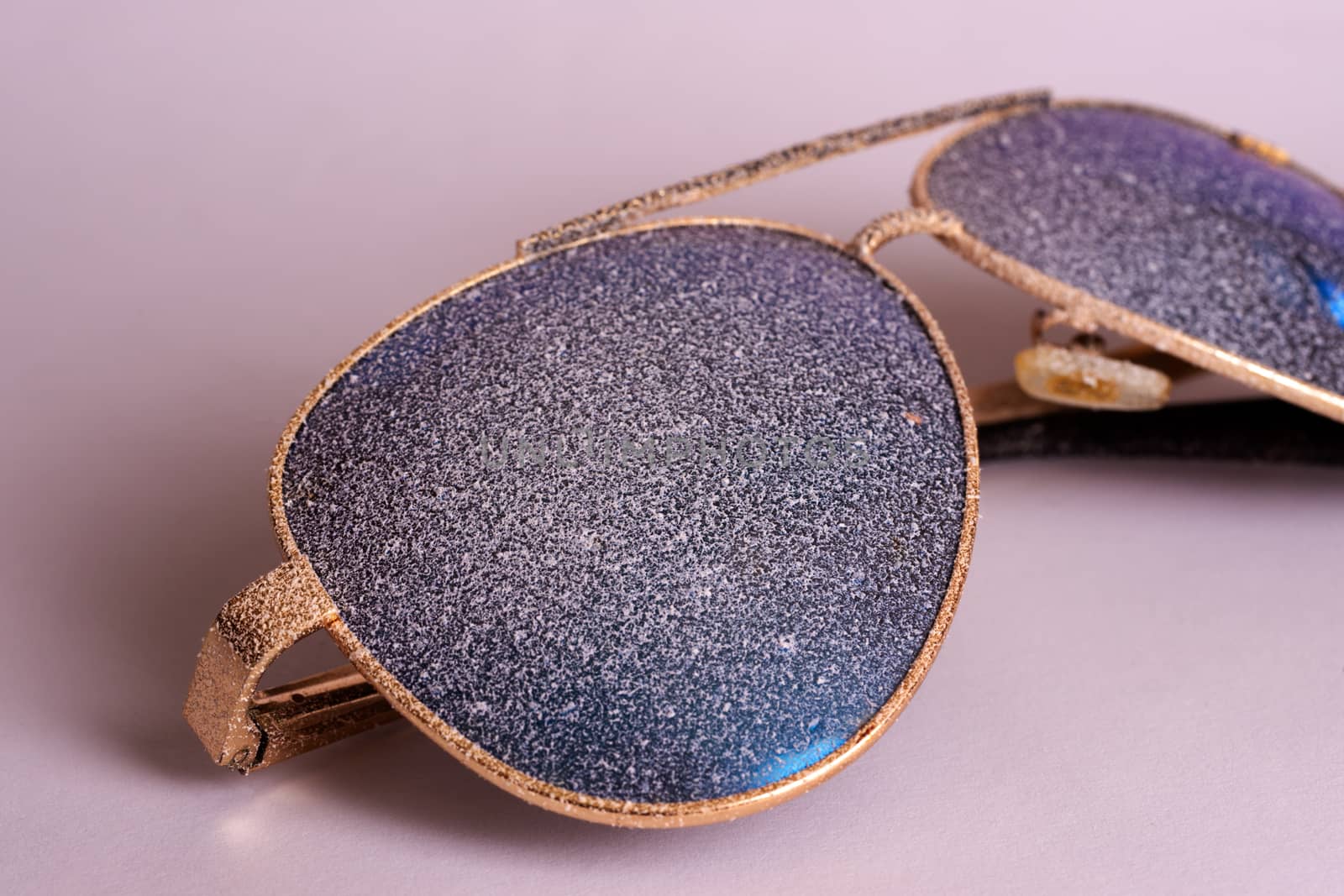 Sunglasses with artificial snow on white-purple background close-up view.