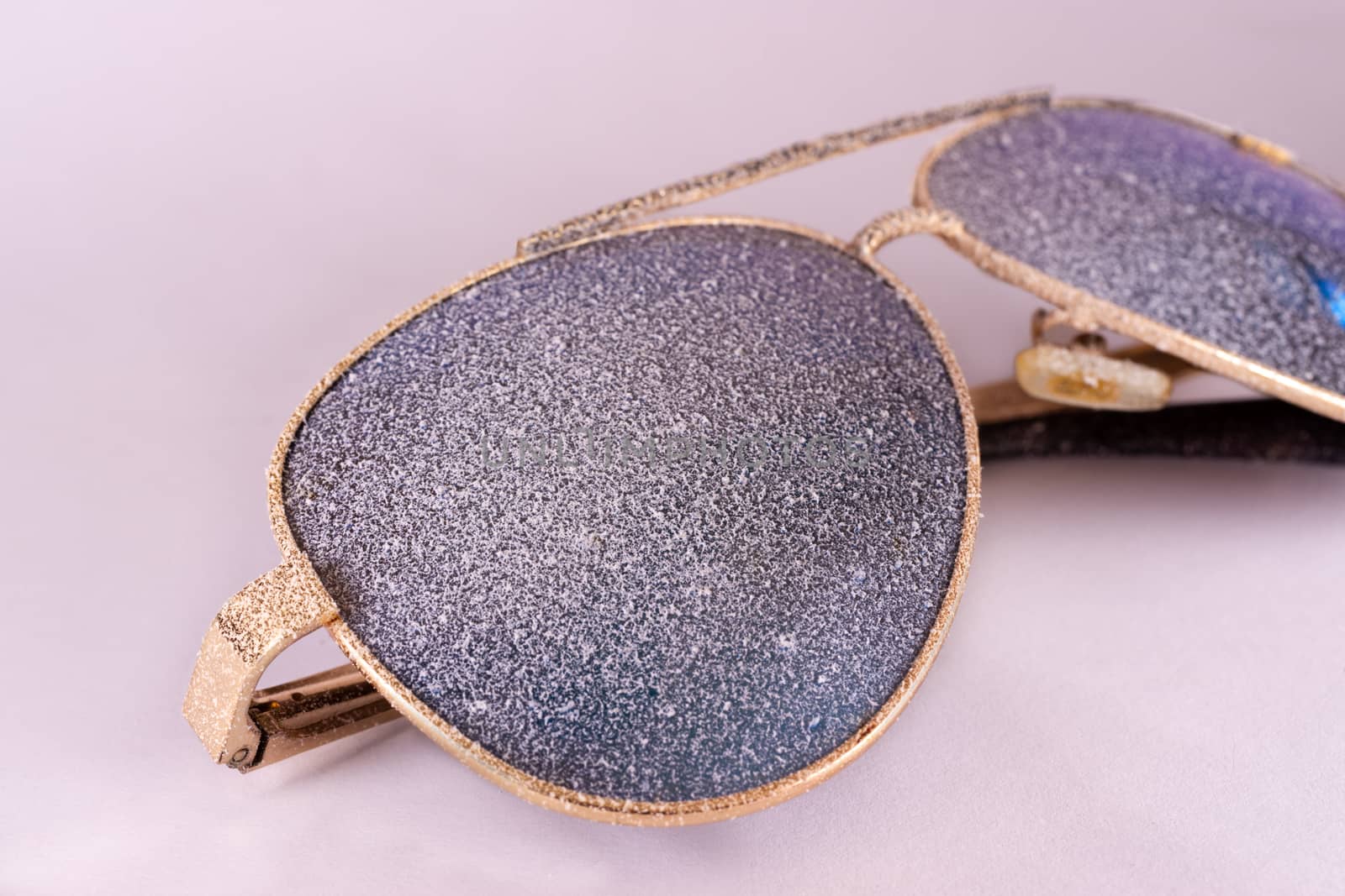 Sunglasses with artificial snow on white-purple background close-up view.