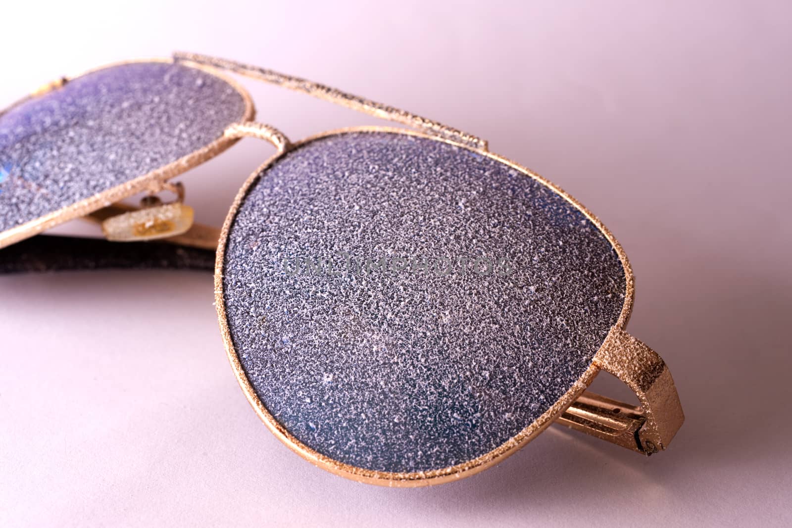 Sunglasses with artificial snow on white-purple background close-up view.