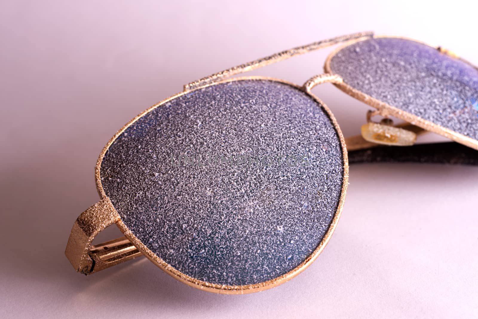 Sunglasses with artificial snow on white-purple background close-up view.