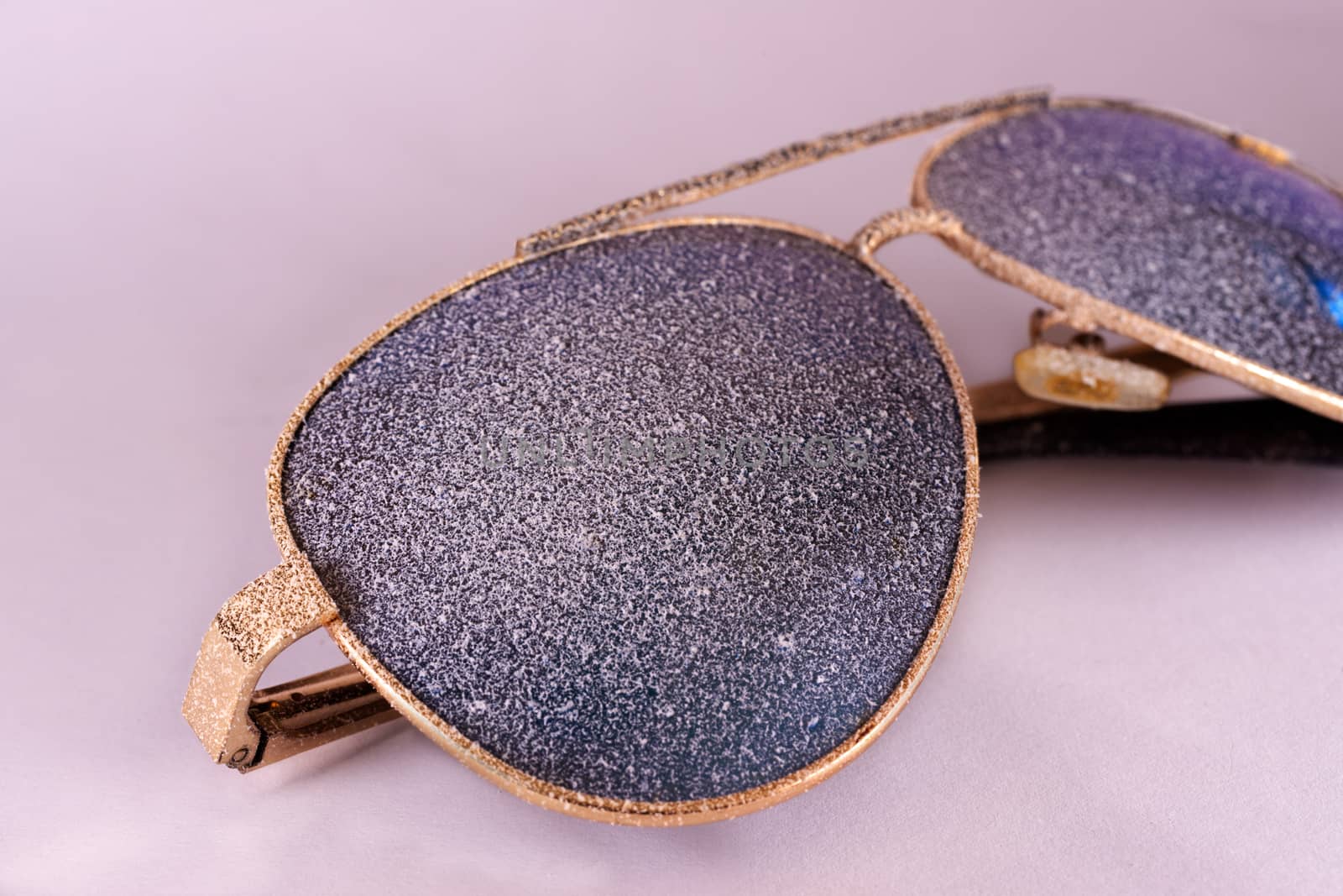 Sunglasses with artificial snow on white-purple background close-up view.