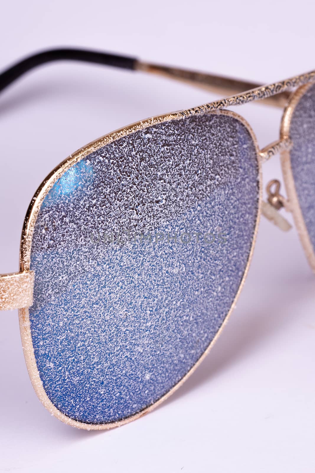 Sunglasses with artificial snow on white-purple background close-up view.