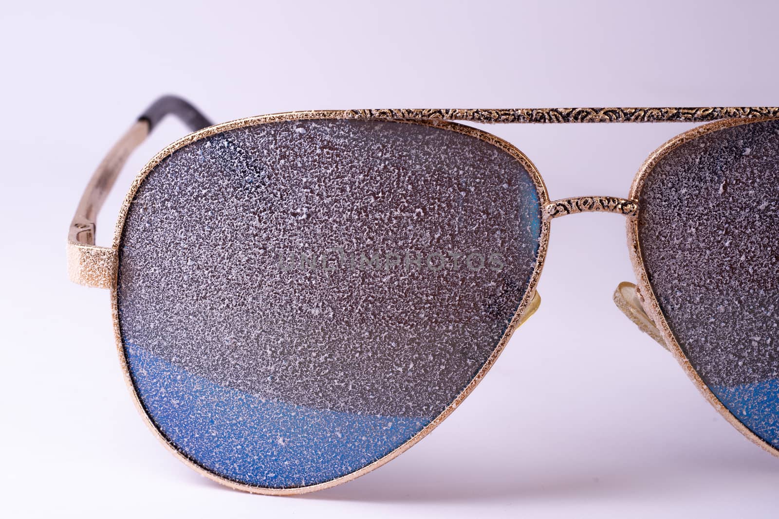 Sunglasses with artificial snow on white-purple background close-up view.