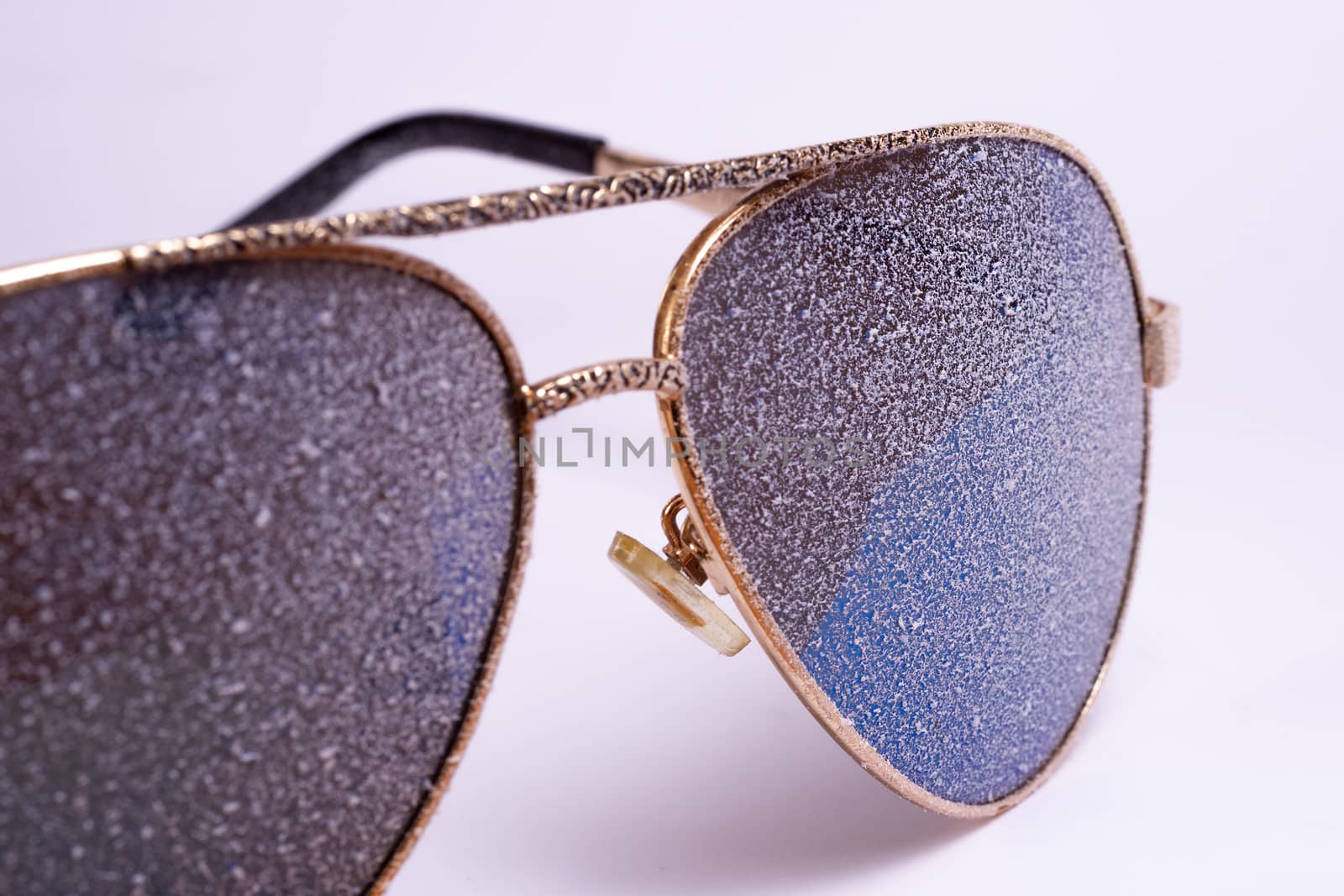 Sunglasses with artificial snow on white-purple background close-up view.