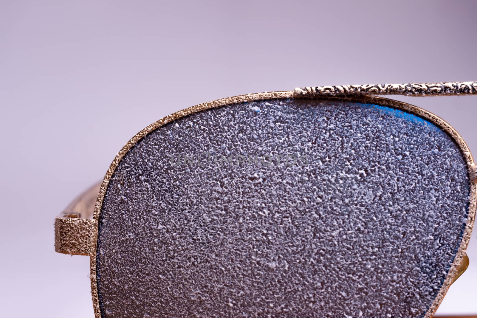 Sunglasses with artificial snow on white-purple background close-up view.