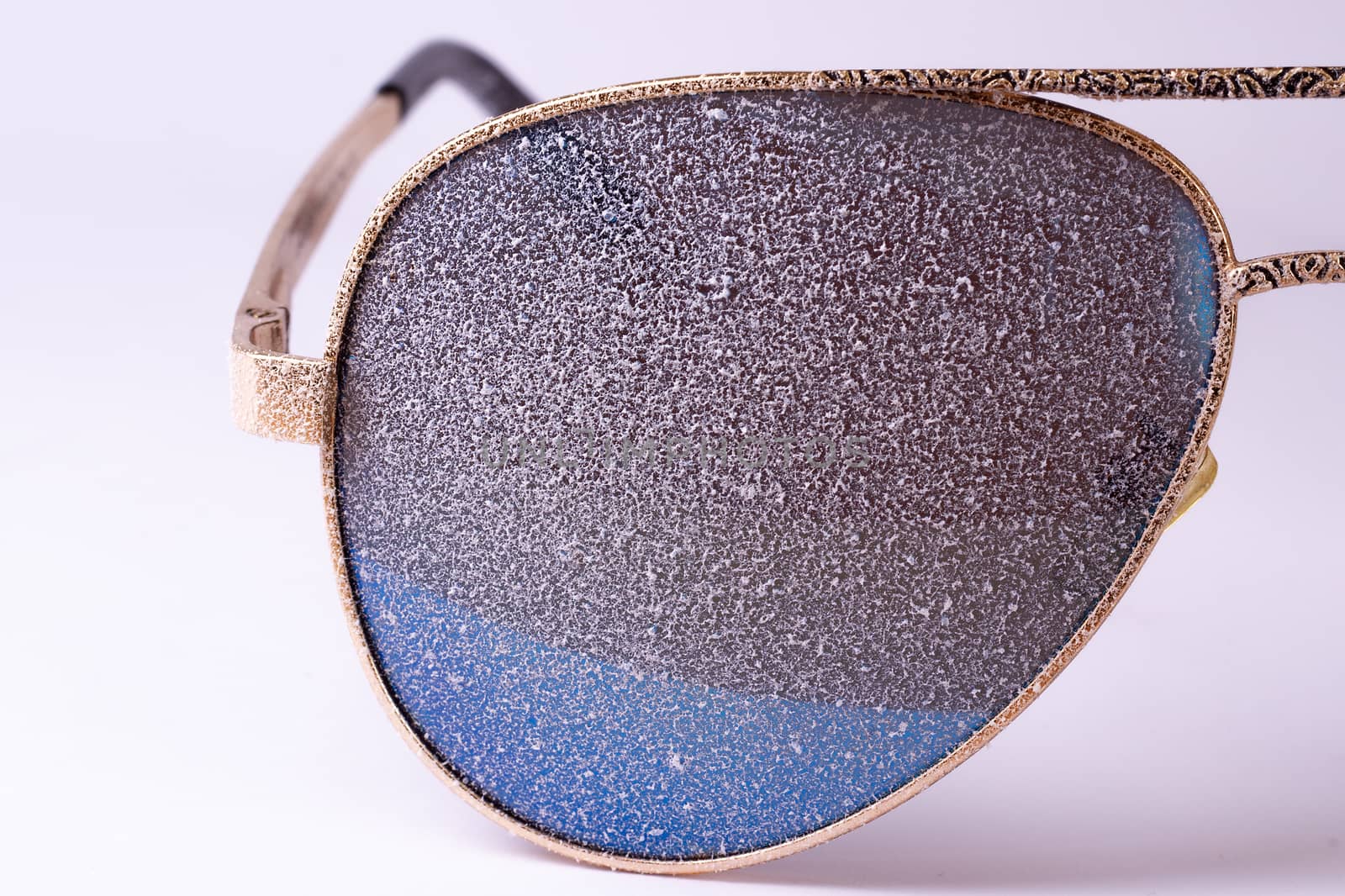 Sunglasses with artificial snow on white-purple background close-up view.