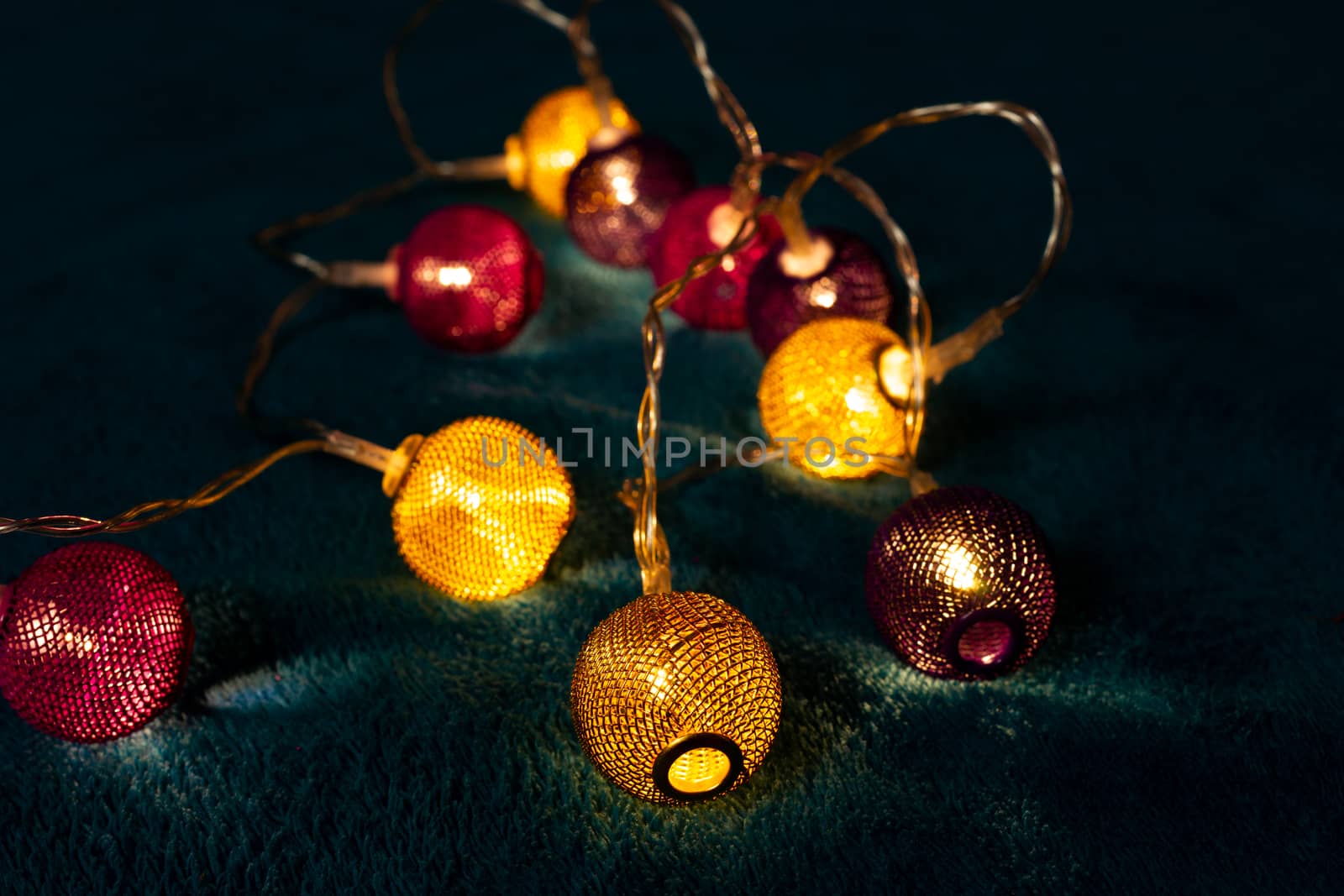 Battery garland with metallic grid balls on blue blanket. Closeup view with blurred background.