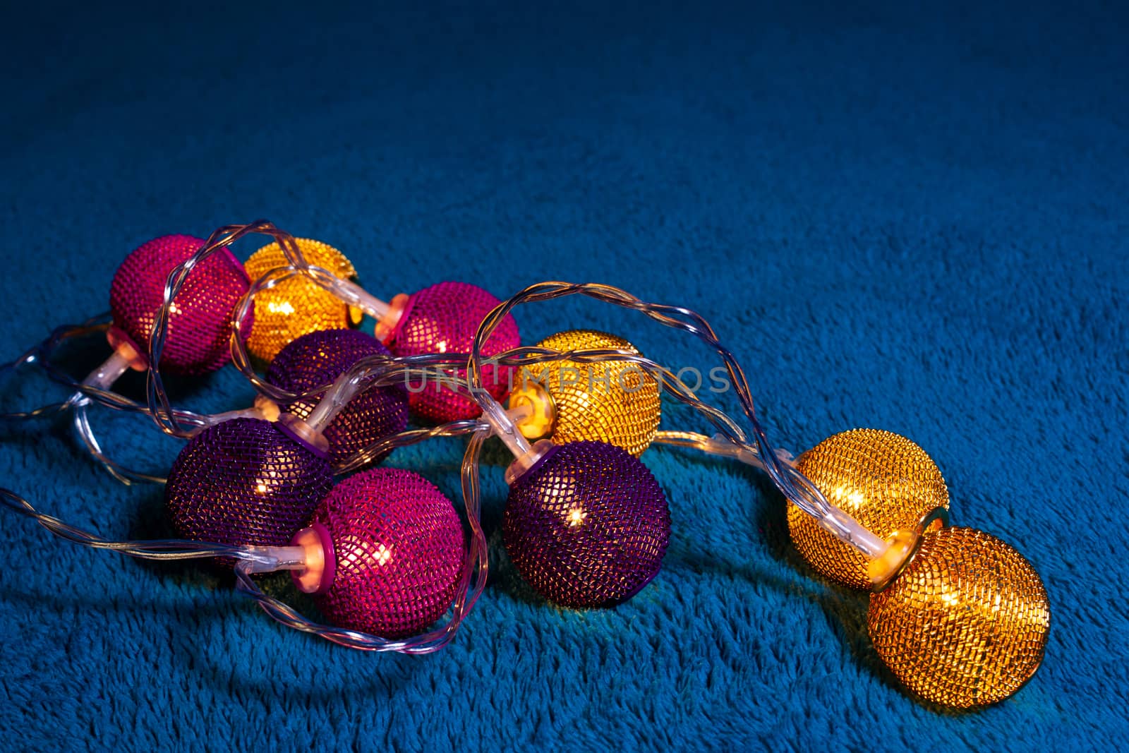 Battery garland with metallic grid balls on blue blanket. Closeup view with blurred background.