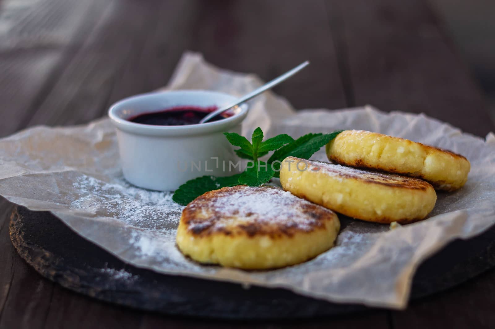 Fried cheesecakes or pancakes on craft paper on stone plate with blueberry jam.