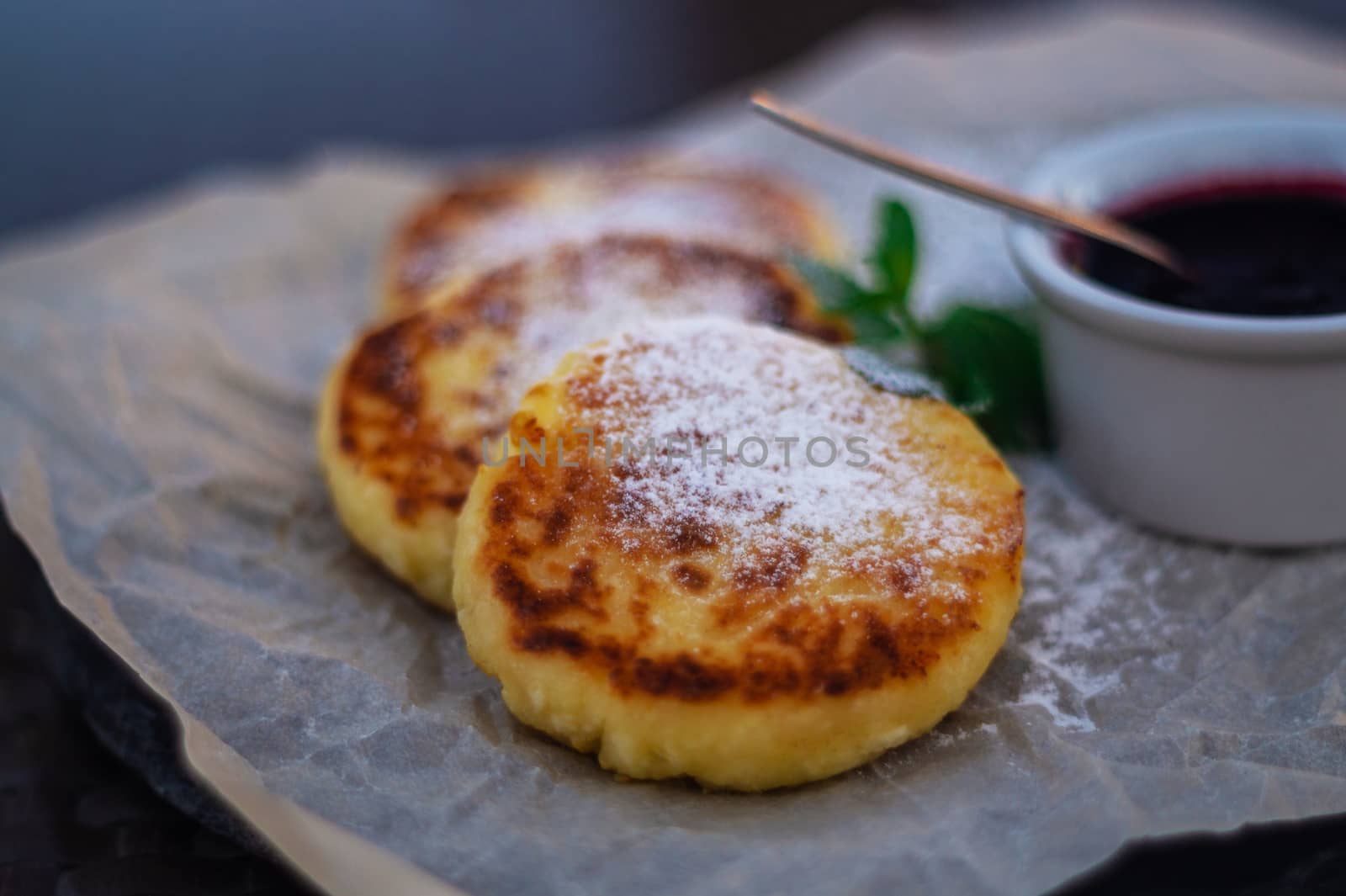 Fried cheesecakes or pancakes on craft paper on stone plate with blueberry jam.