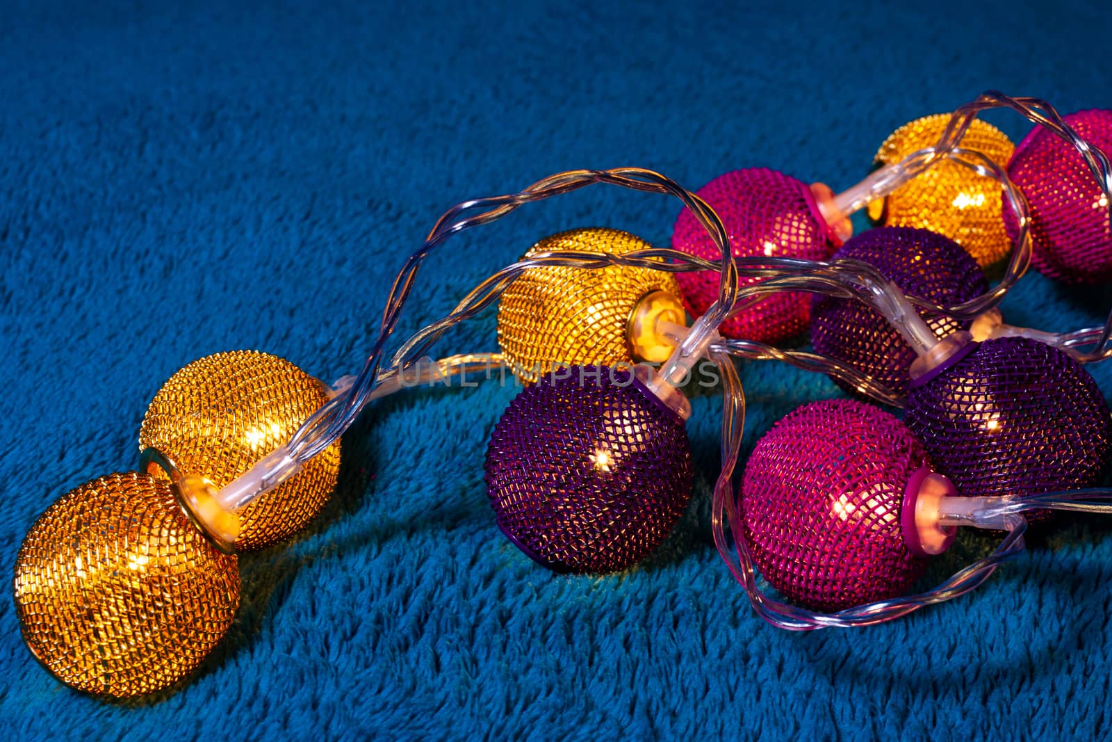 Battery garland with metallic grid balls on blue blanket. Closeup view with blurred background.