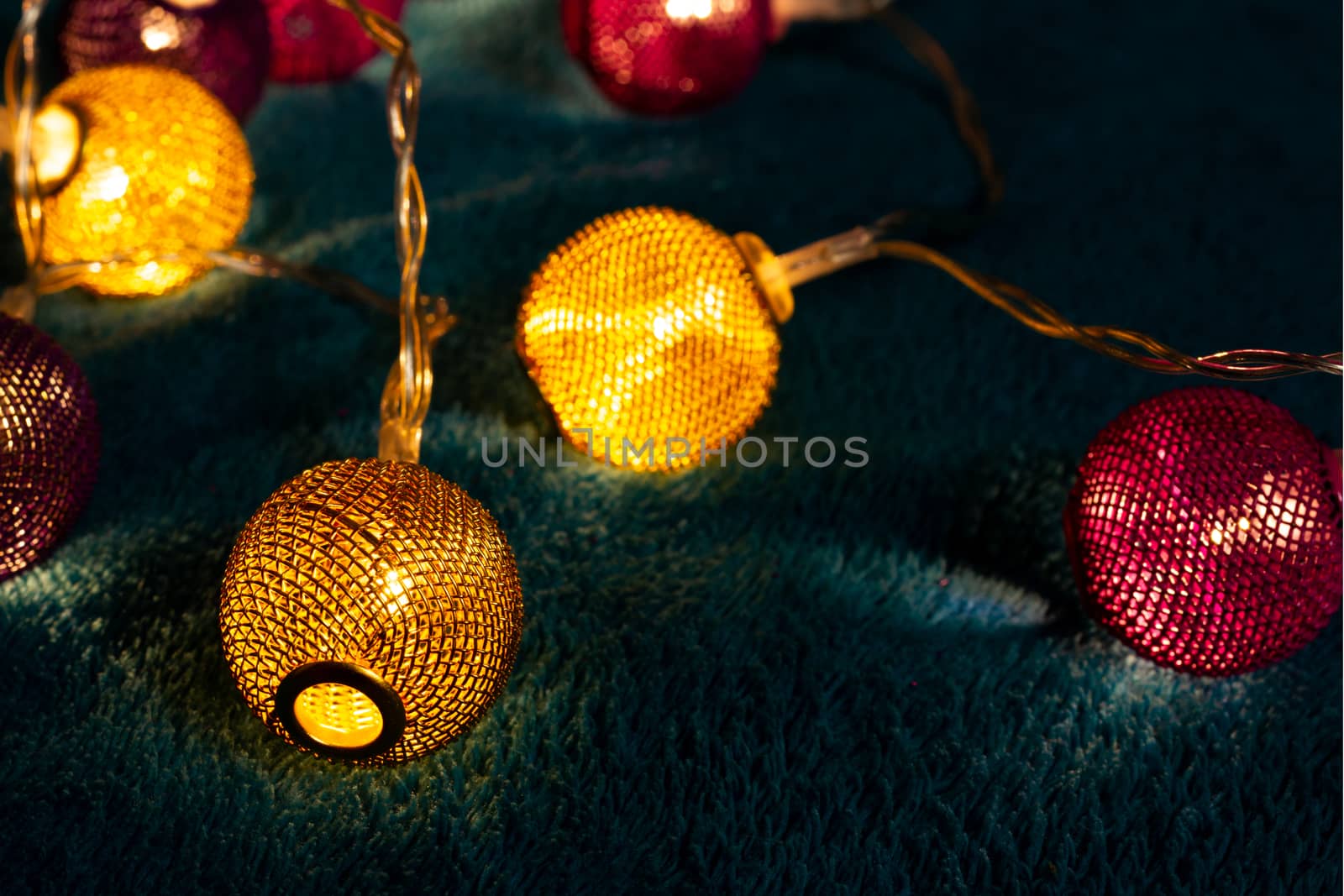 Battery garland with metallic grid balls on blue blanket. Closeup view with blurred background.