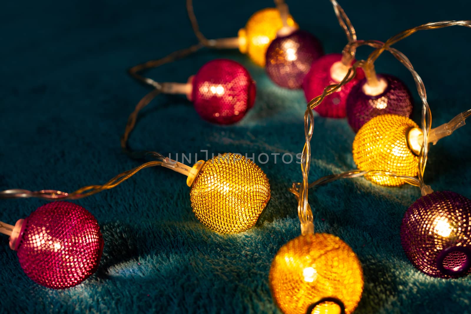 Battery garland with metallic grid balls on blue blanket. Closeup view with blurred background.