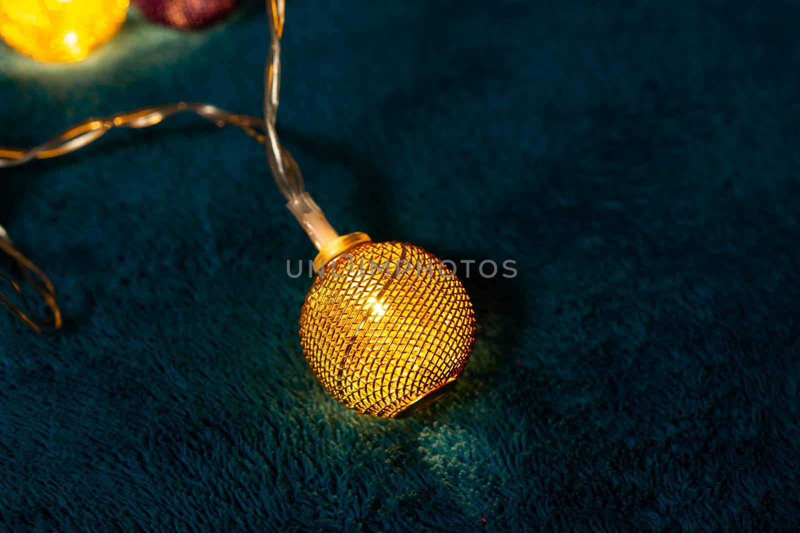 Battery garland with metallic grid balls on blue blanket. Closeup view with blurred background.