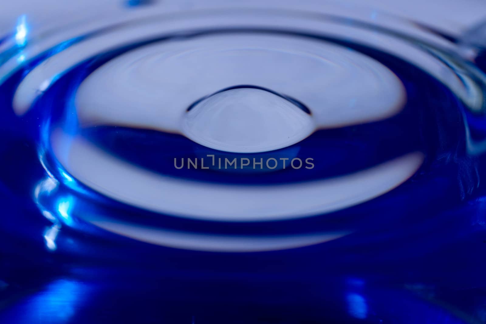 Waves on water surface in blue glass. Drop falling and splashing in water. Soft focus photo.