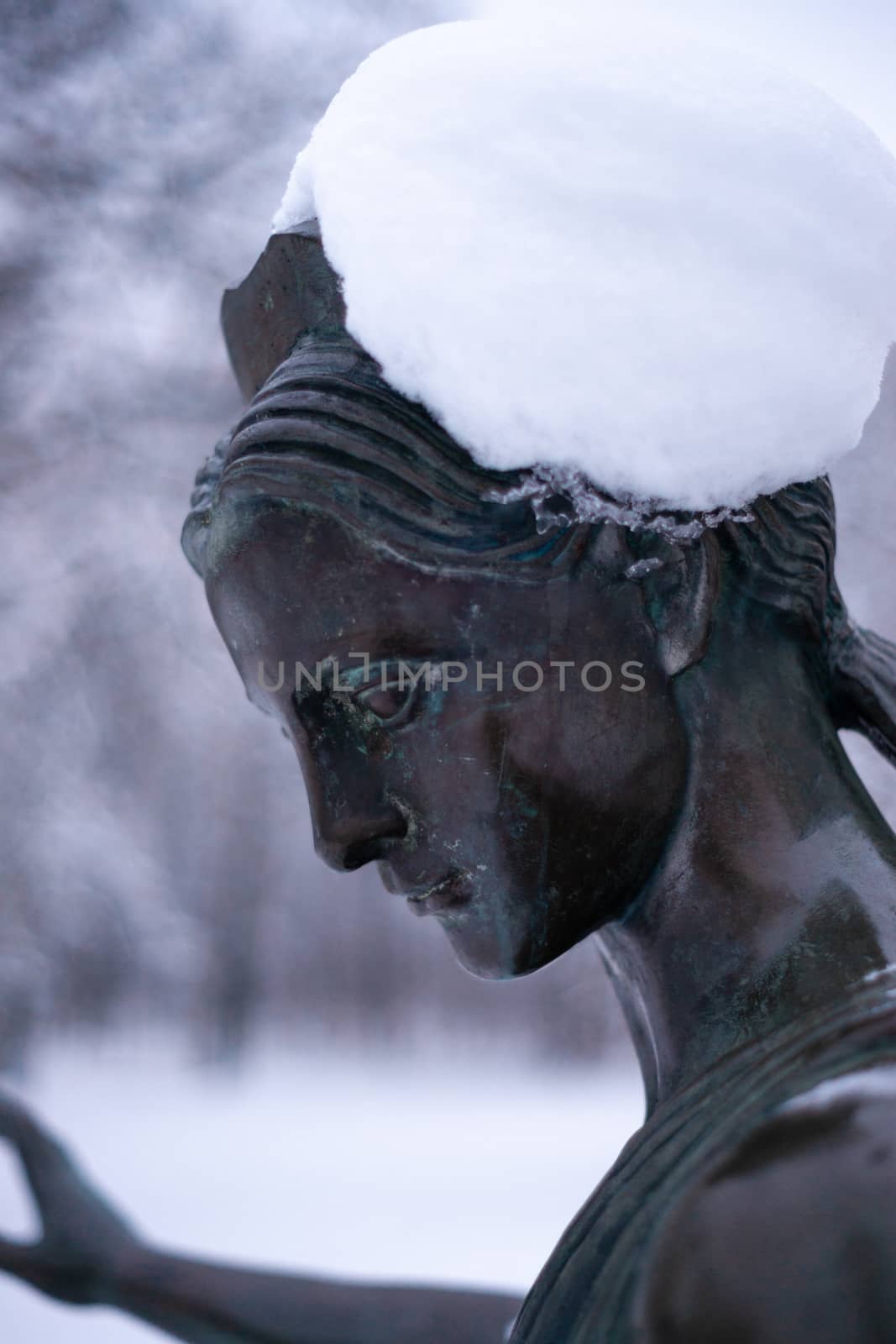 Bronze monument of a woman in winter snow park. Closeup with blurred background.