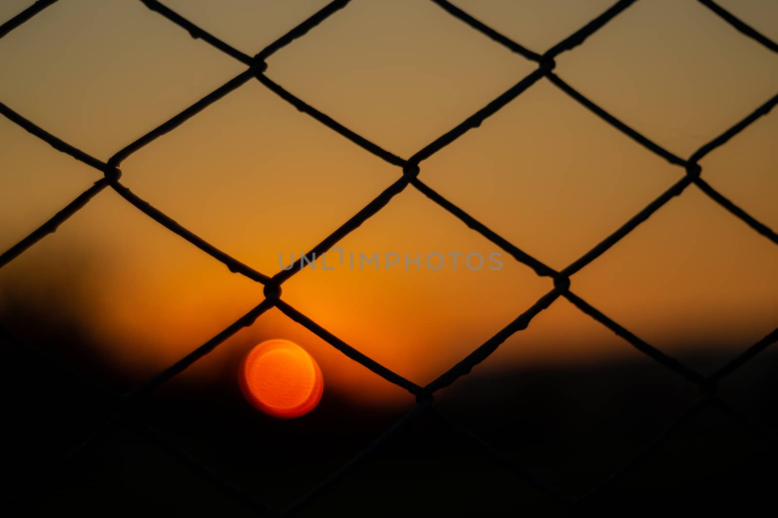 Orange evening sky with blurred sun on horizon trough fence. Creative idea- underexposed photo. by alexsdriver