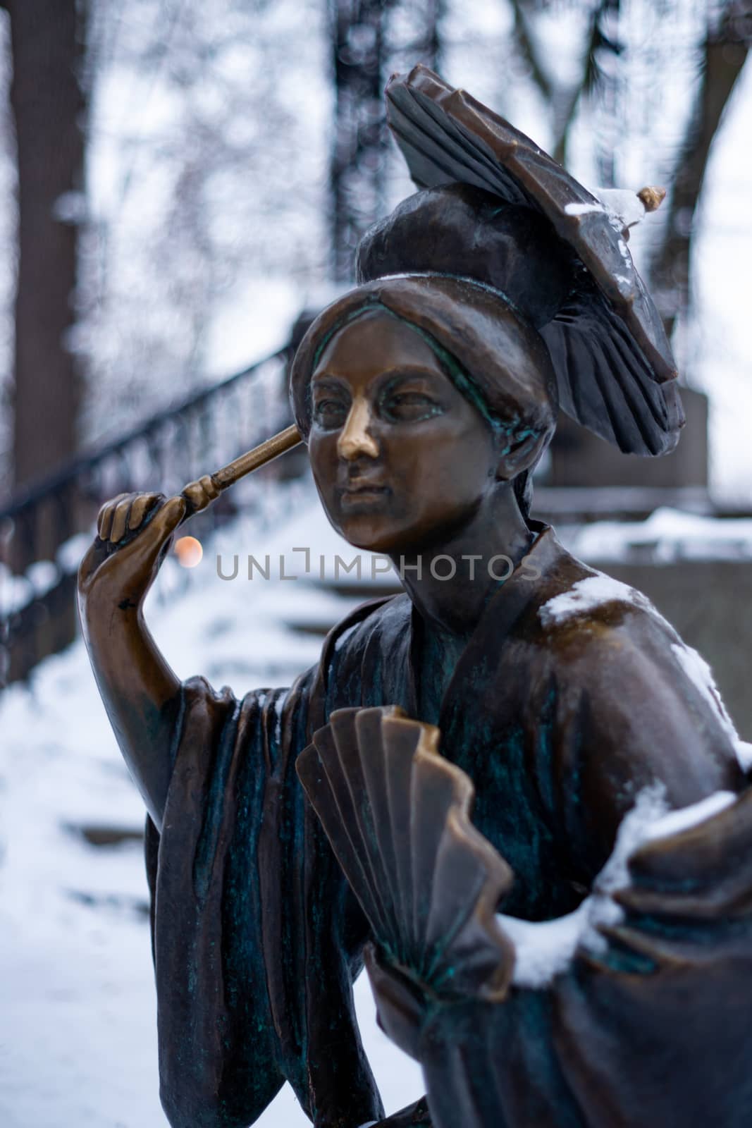 Bronze monument of a chinese old man with umbrella in winter snow park. Closeup with blurred background.