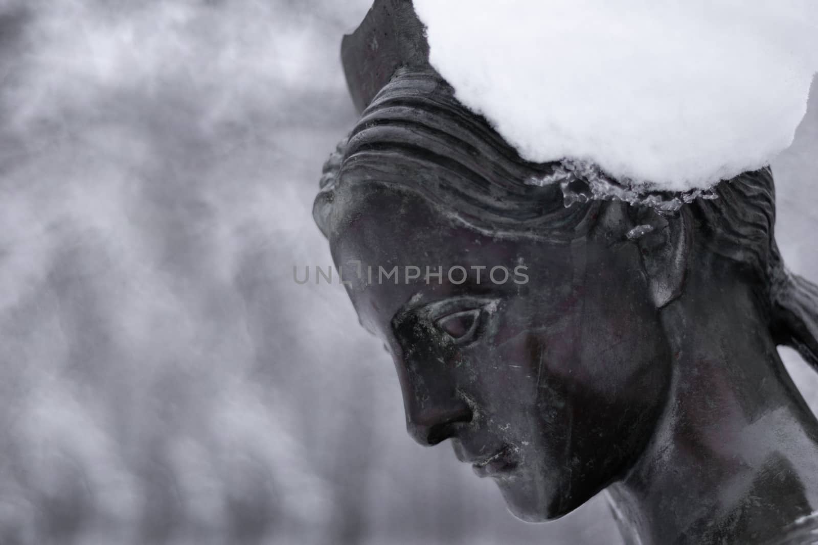 Bronze monument of a woman in winter snow park. Closeup with blurred background.