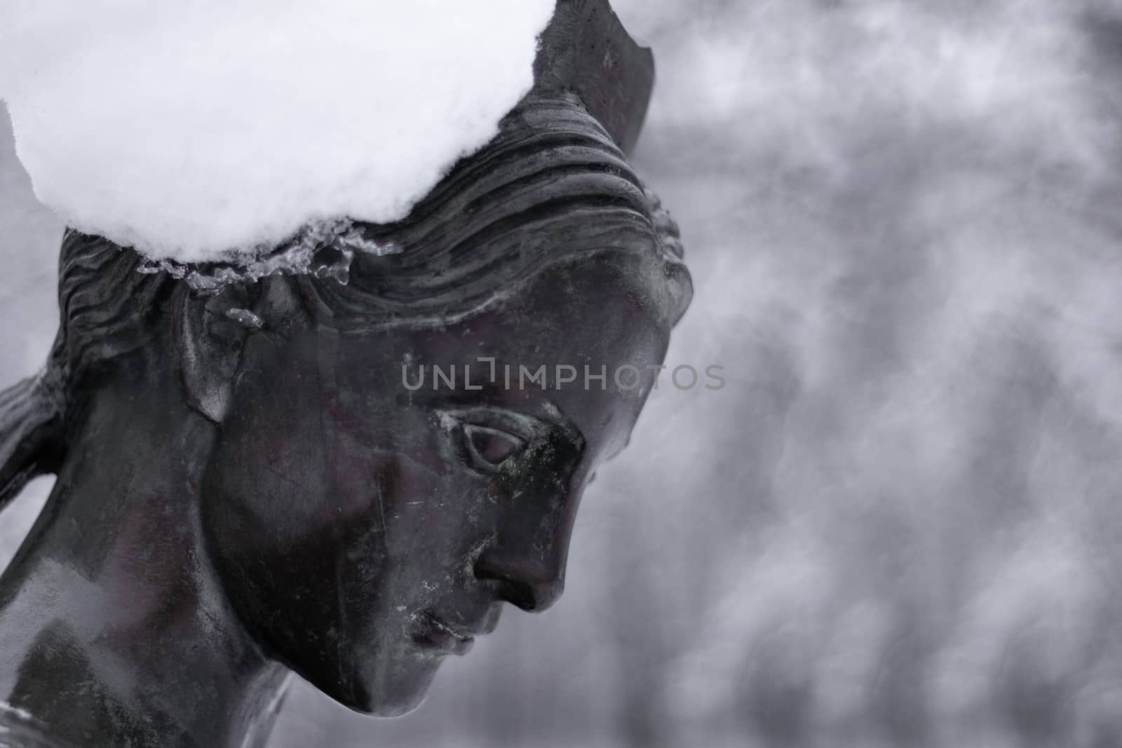 Bronze monument of a woman in winter snow park. Closeup with blurred background.