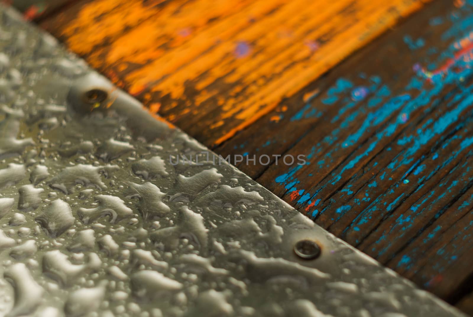 The metal sheet on the left and the boards are orange and blue on the right. Rain drops on metal and wood. The photo shows a part of a children's hill