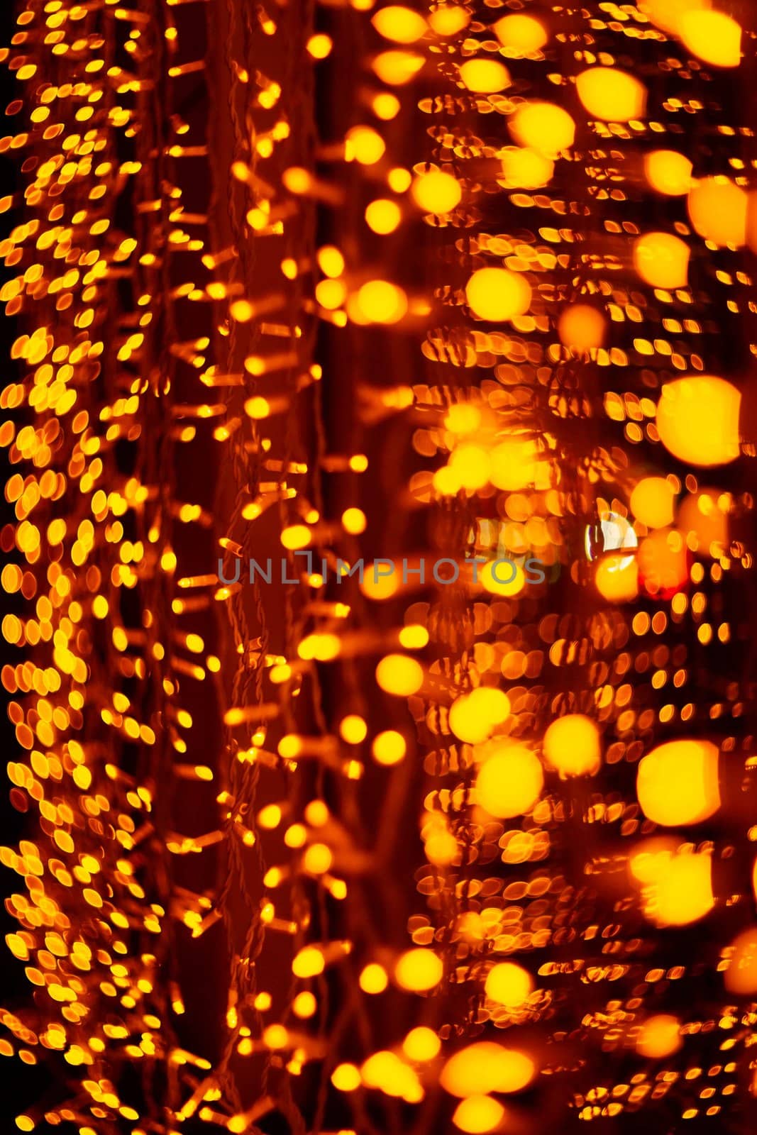 Vertical Christmas garland wall on glass window. Light is orange and defocused. Blurred background, new year mood.