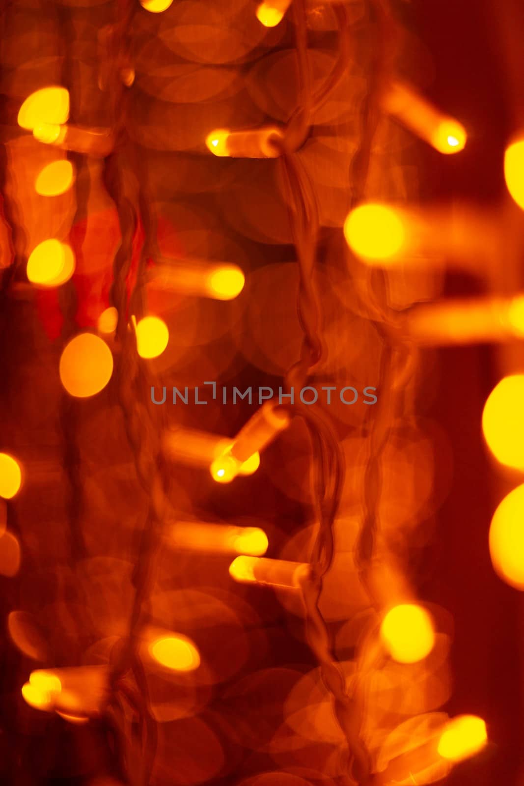 Vertical Christmas garland wall on glass window. Light is orange and defocused. Blurred background, new year mood.