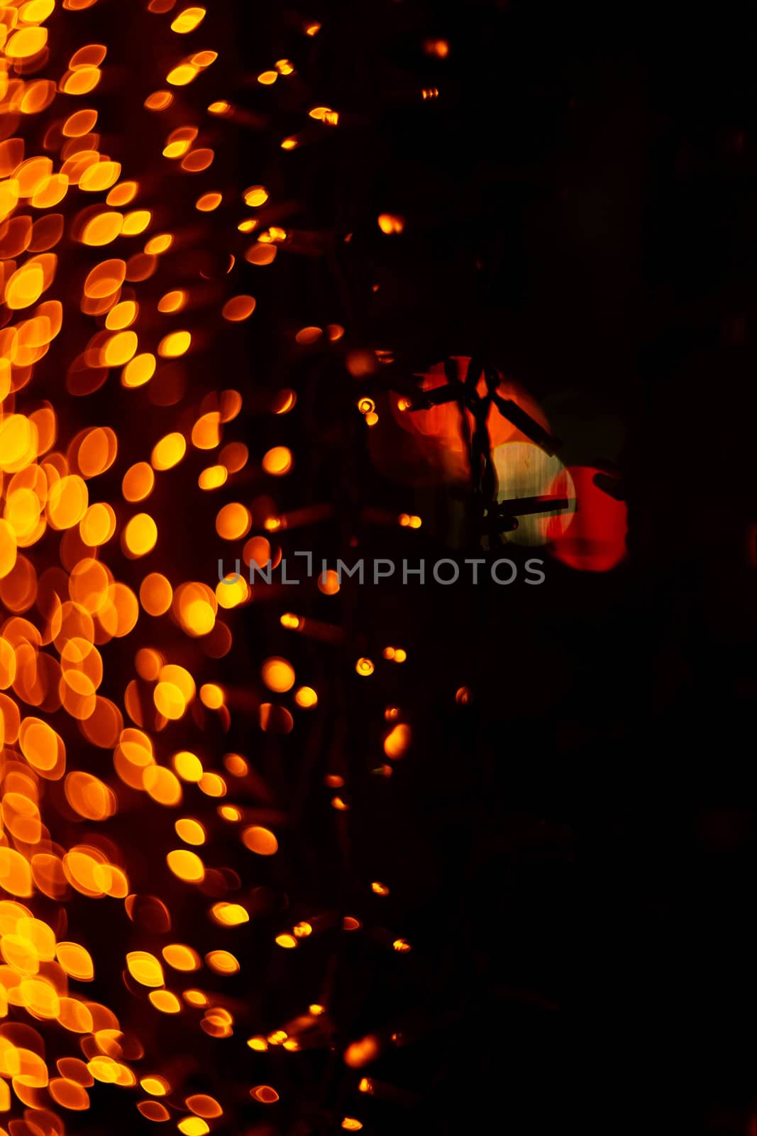 Vertical Christmas garland wall on glass window. Light is orange and defocused. Blurred background, new year mood.