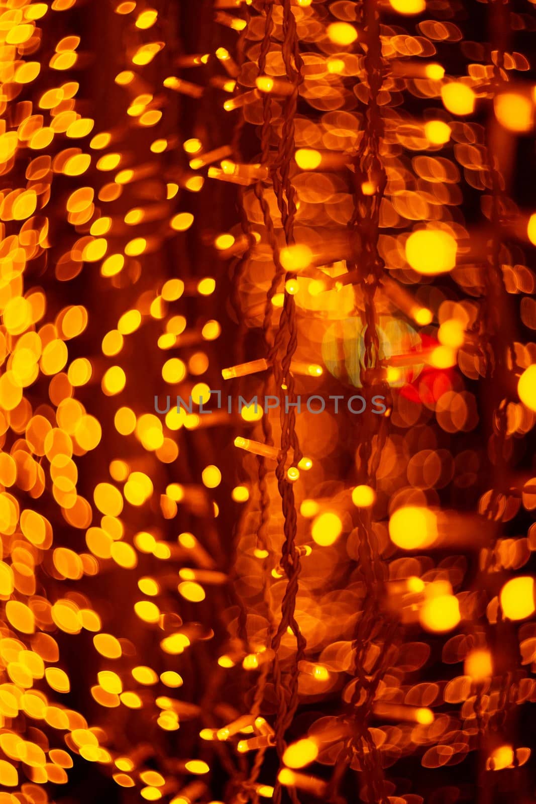 Vertical Christmas garland wall on glass window. Light is orange and defocused. Blurred background, new year mood.