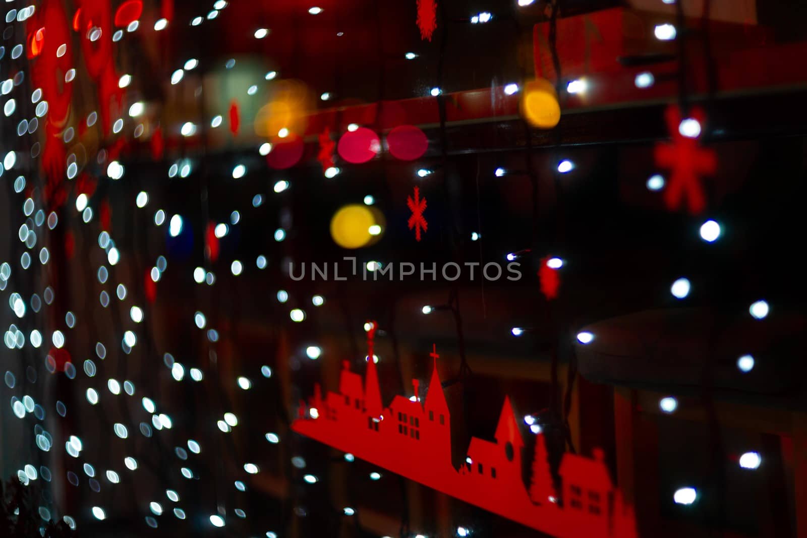 Vertical Christmas garland wall on glass window. Light is white and defocused. Blurred background, new year mood.
