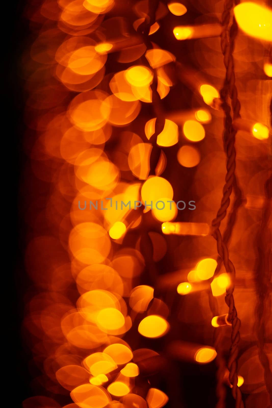 Vertical Christmas garland wall on glass window. Light is orange and defocused. Blurred background, new year mood.