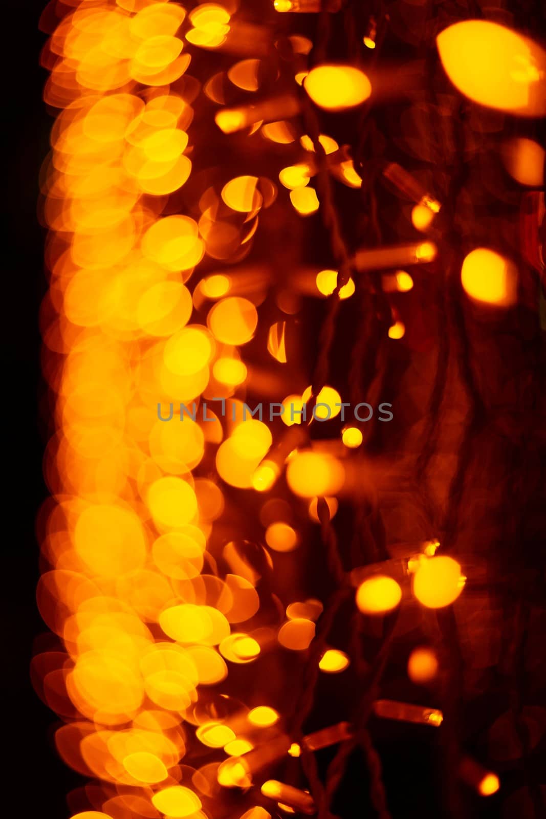 Vertical Christmas garland wall on glass window. Light is orange and defocused. Blurred background, new year mood.