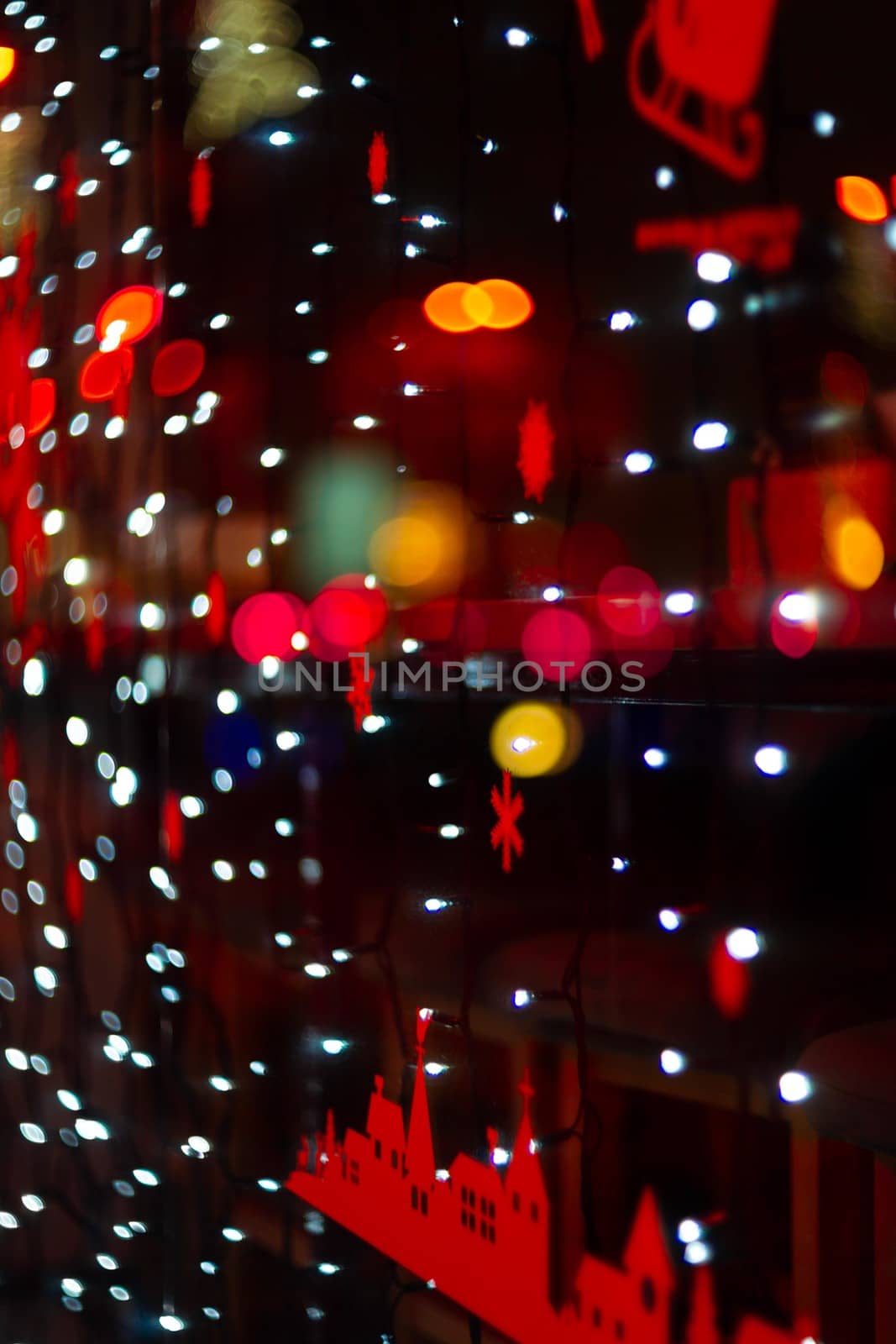 Vertical Christmas garland wall on glass window. Light is white and defocused. Blurred background, new year mood.