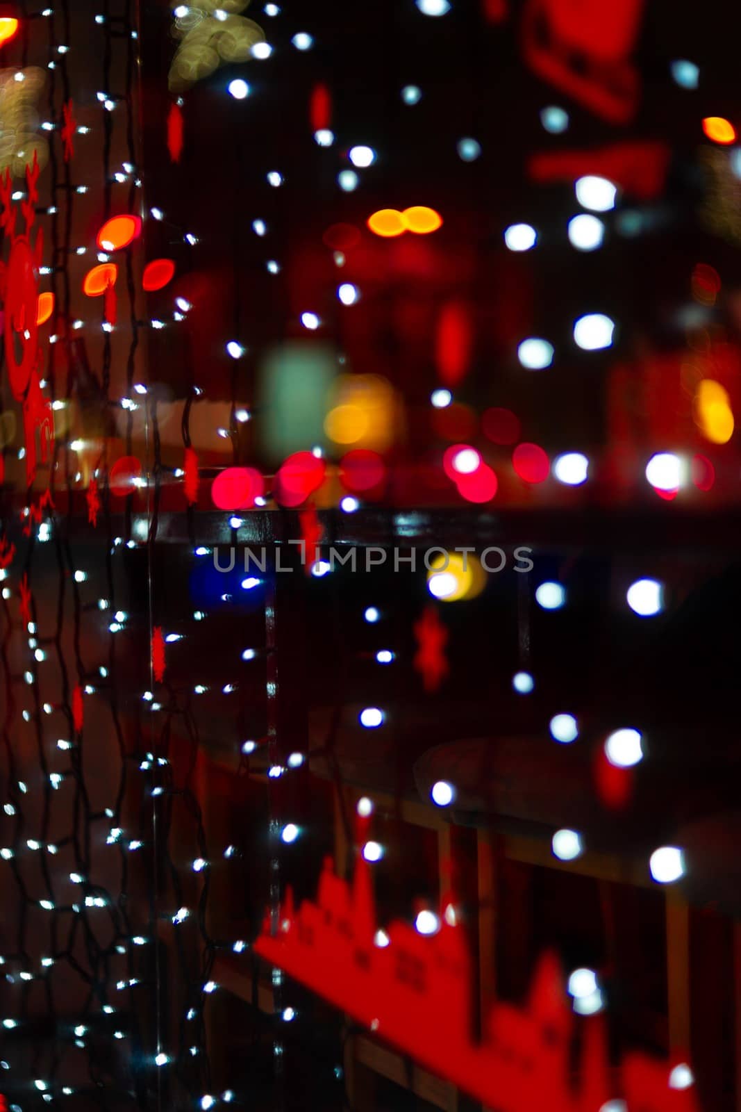 Vertical Christmas garland wall on glass window. Light is white and defocused. Blurred background, new year mood.