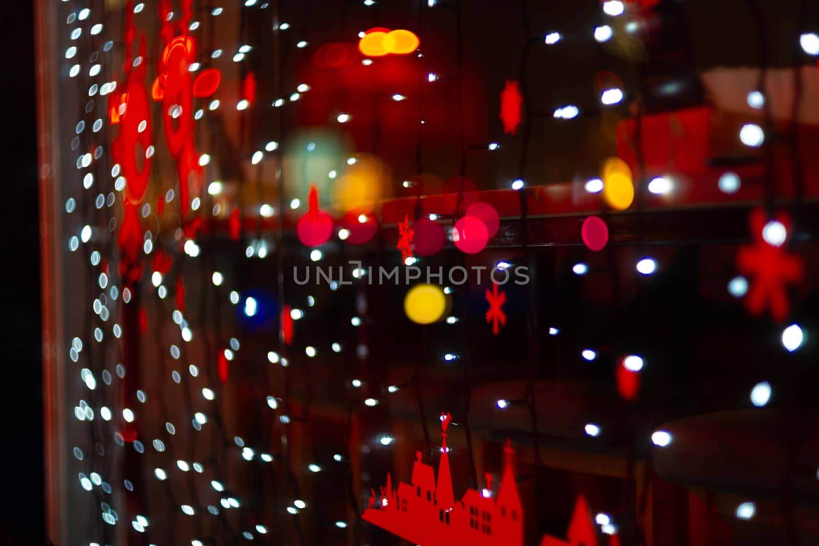 Vertical Christmas garland wall on glass window. Light is white and defocused. Blurred background, new year mood.