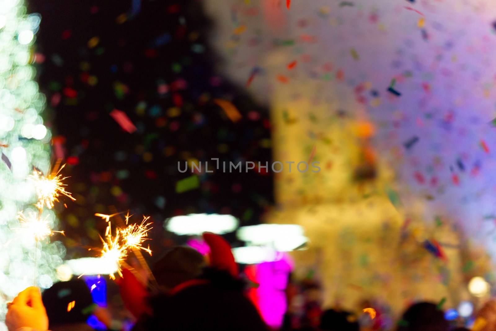 New Year celebration on main square. A lot of smoke or fog, lights, salute and confetti. Blurred colorful background. Bengali fire in hand with glove on foreground. Concert scene with blue light at right side of frame.