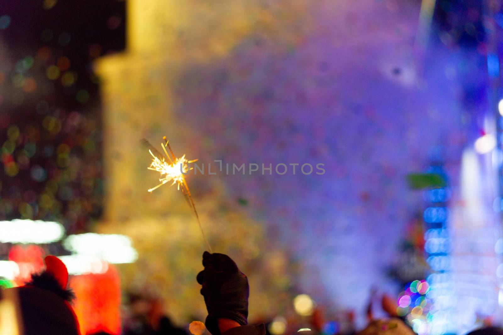 New Year celebration on main square. A lot of smoke or fog, lights, salute and confetti. Blurred colorful background. Bengali fire in hand with glove on foreground. Concert scene with blue light at right side of frame.