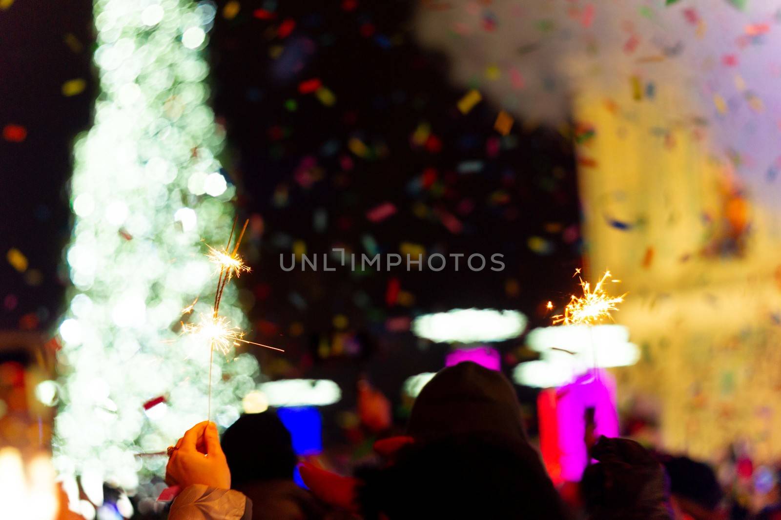 New Year celebration on main square. A lot of smoke or fog, lights, salute and confetti. Blurred colorful background. Bengali fire in hand with glove on foreground. Concert scene with blue light at right side of frame.