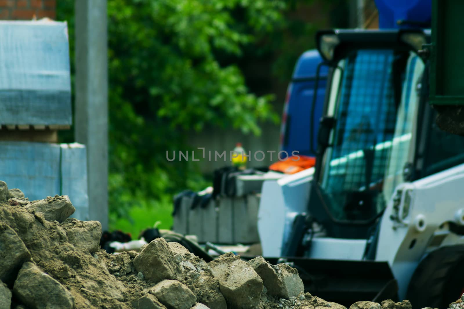 a pile of rubble and soil in the foreground. in the background a mini bulldozer loader and a truck