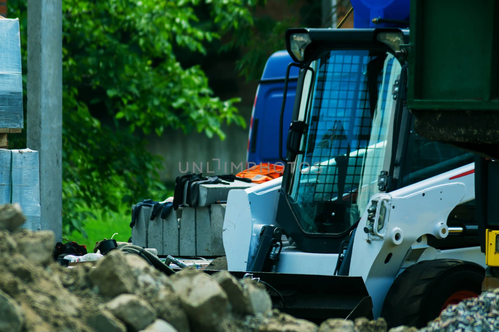 a pile of rubble and soil in the foreground. in the background a mini bulldozer loader and a truck