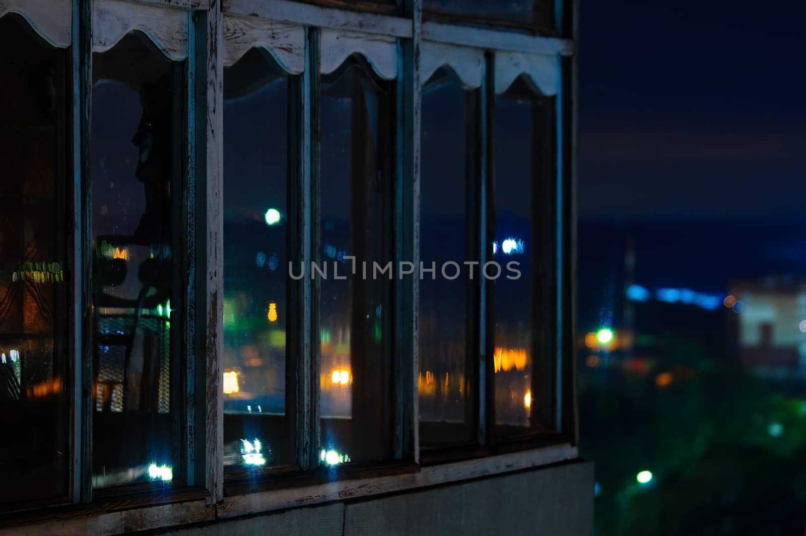 Long exposure cityscape night photo. Balcony with windows let through the lights of the night city.