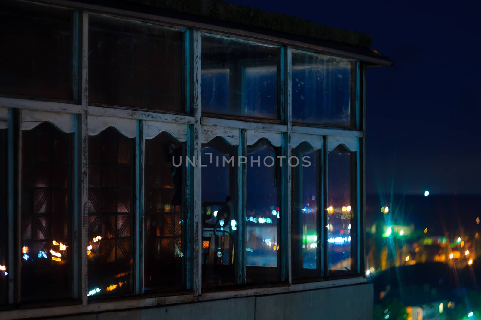 Long exposure cityscape night photo. Balcony with windows let through the lights of the night city.