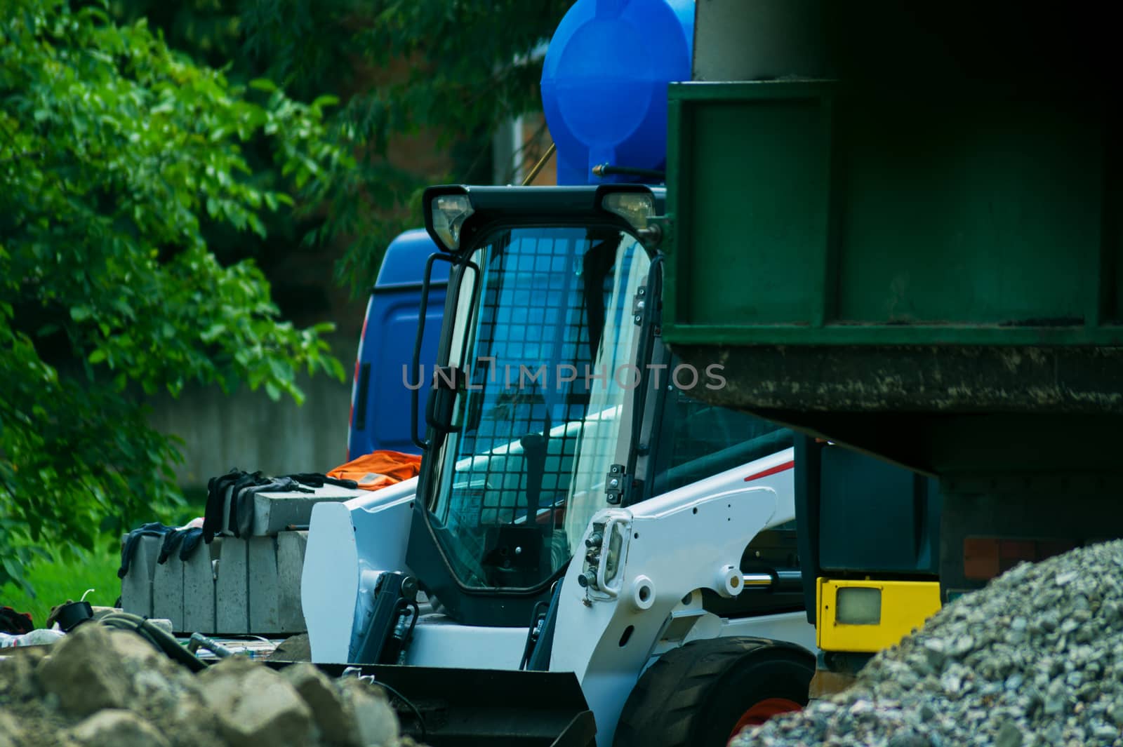 a pile of rubble and soil in the foreground. in the background a mini bulldozer loader and a truck