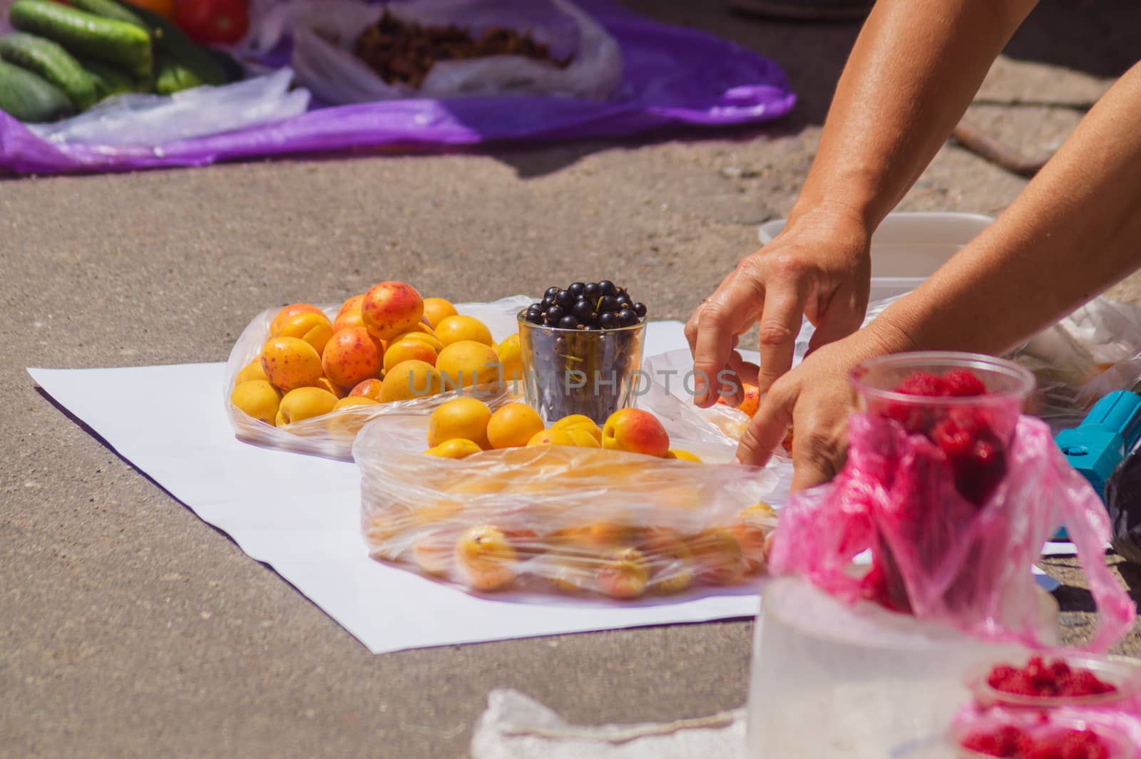 Street spontaneous mart on the asphalt. An old woman straightens vegetables on white cloth.